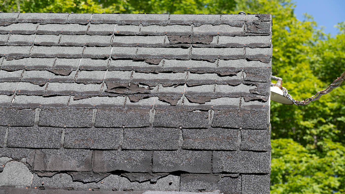 Badly damaged shingle roof with missing and broken shingles before replacement