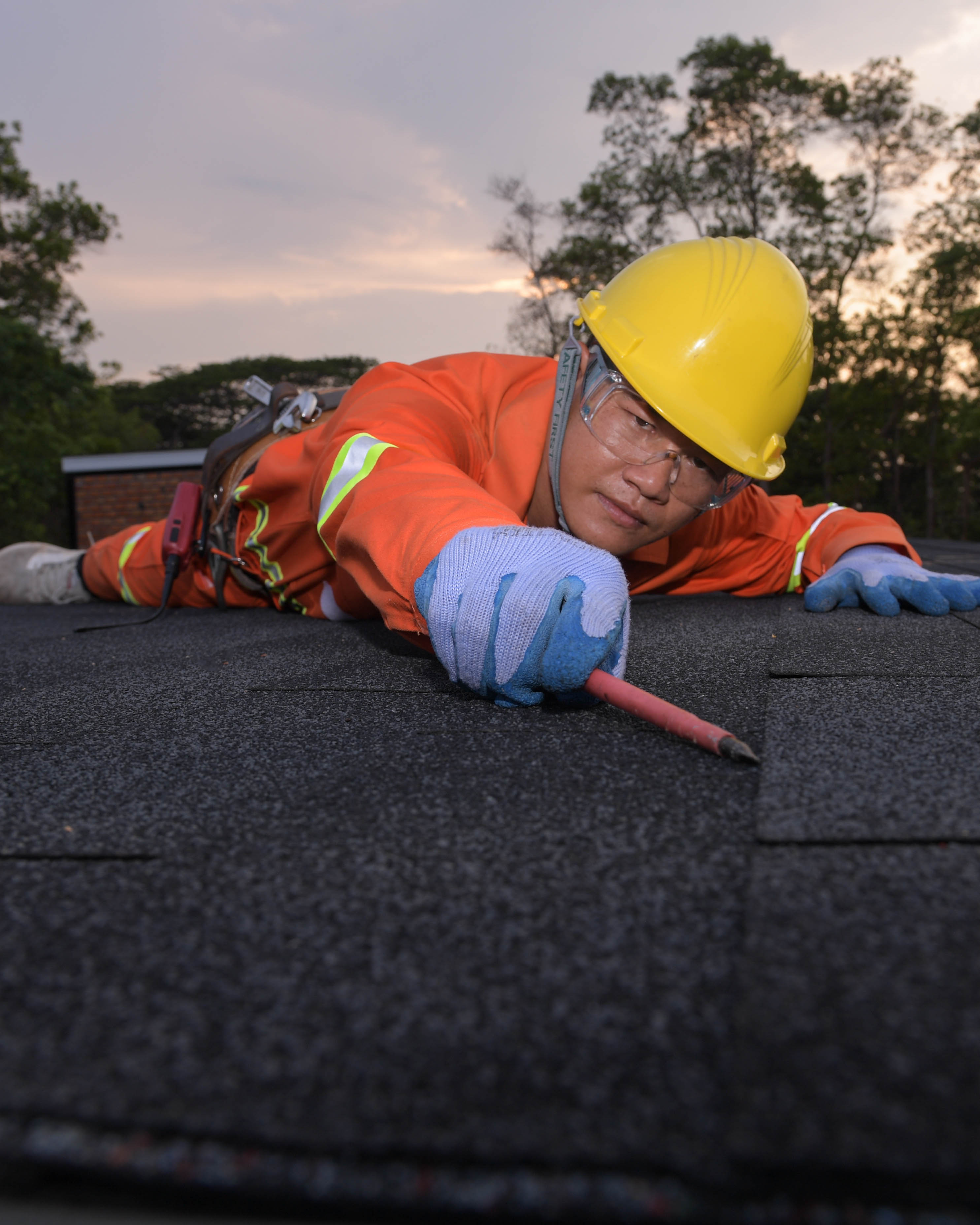 Roofer in protective gear replacing shingles on a residential roof